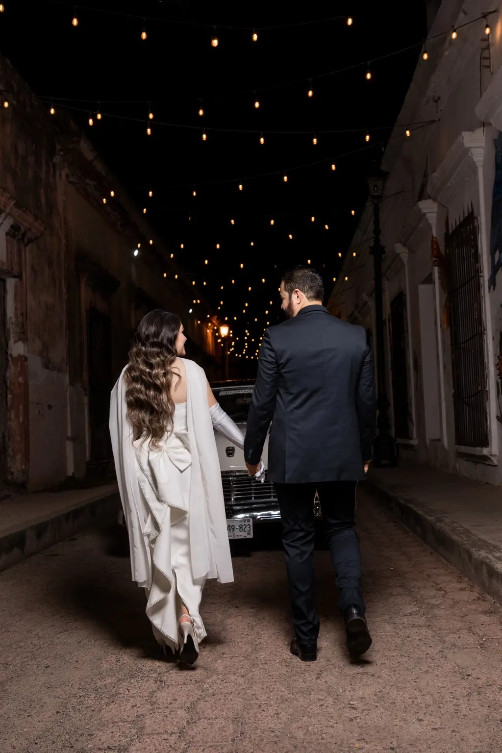 Martha Karina y Elve Jesús caminando de la mano por una calle iluminada